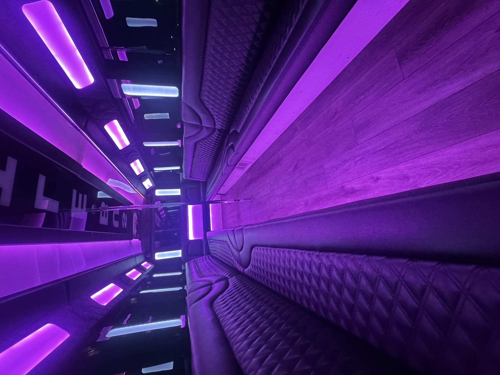 The Titan party bus interior with purple LED lighting, diamond-stitched leather seating and dance pole